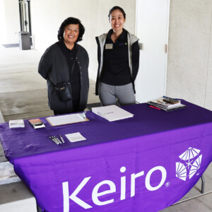 two people smiling at a table with a tablecloth that reads "Keiro"