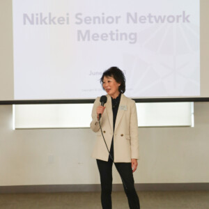 woman talking into microphone, presentation behind her reads "Nikkei Senior Network Meeting"