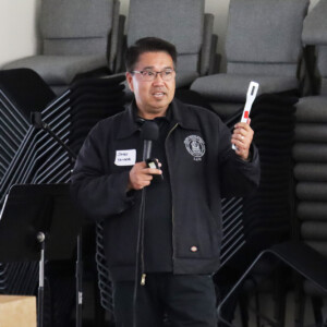 man talking into microphone holding a tool