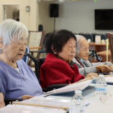 four women sitting at a table reading a from a binder