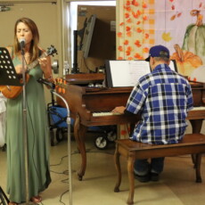 man playing at piano and woman singing while playing ukulele