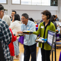 a man in blue and a woman in green handing out bentos