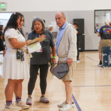 a woman in white with clipboard talking to a man and woman