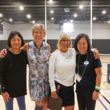 four woman with hands over their shoulders smiling