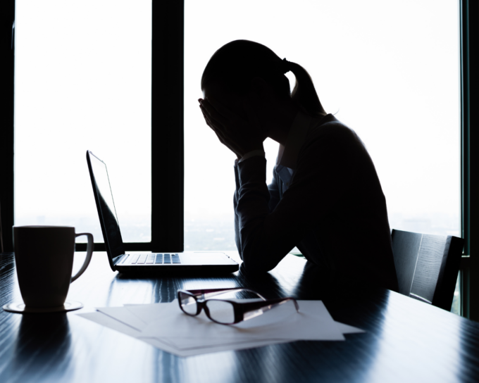 silhouette of person sitting at table stressed with hands on face