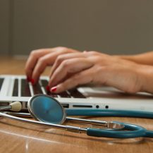 someone typing in a laptop with a stethoscope next to them